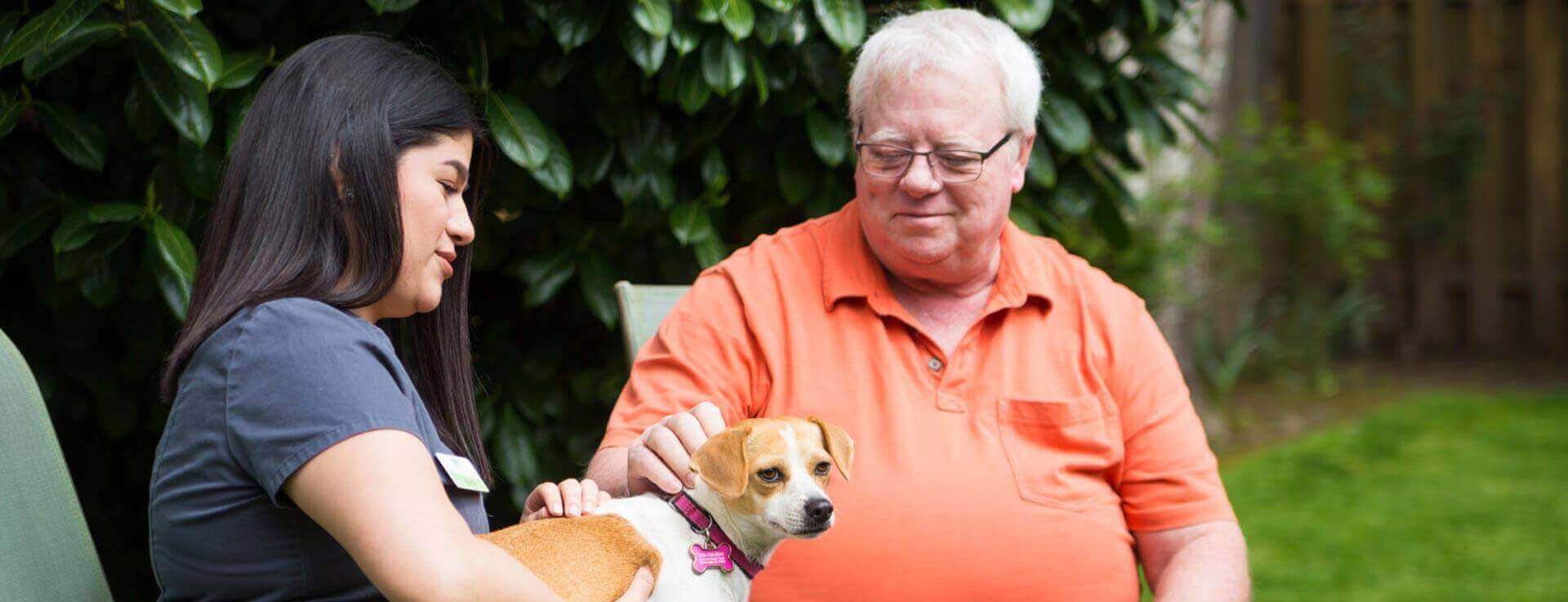 Caregiver and man sitting outside petting puppy