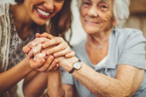 Smiling caregiver clasps hands with dementia client