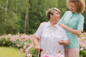 Caregiver And Elderly Person With A Cane In A Garden