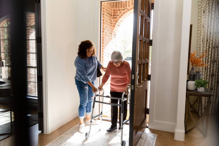 Caregiver assisting aging adult inside their home by holding door open