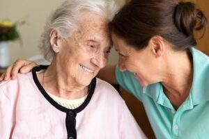 Caregiver smiles while placing arm around Alzheimer’s client in home setting