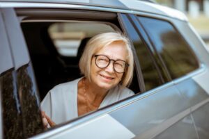 Elderly client riding in transportation vehicle while sticking head out window and smiling 