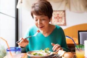 Elderly client sitting at table to eat healthy dish prepared by in-home caregiver 