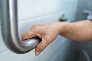Aging adult grabbing hand rail next to toilet in bathroom 