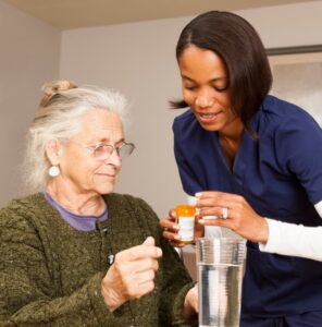 Home caregiver handing pills to older patient to take with glass of water