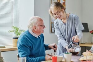 Younger caregiver pouring coffee in older person’s cup 
